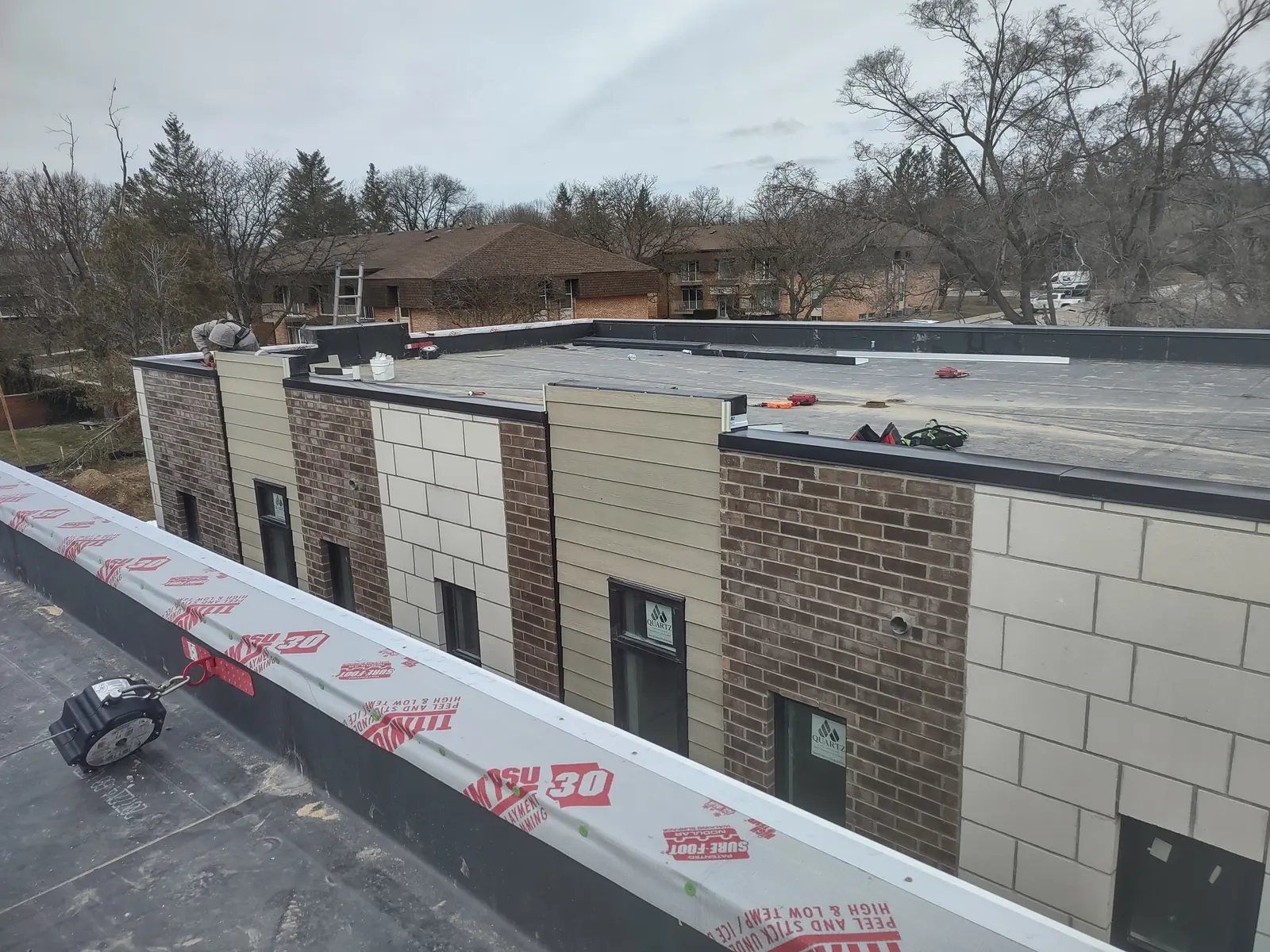 Commercial flat roof installation in progress on modern brick building with peel and stick underlayment, Metro Detroit