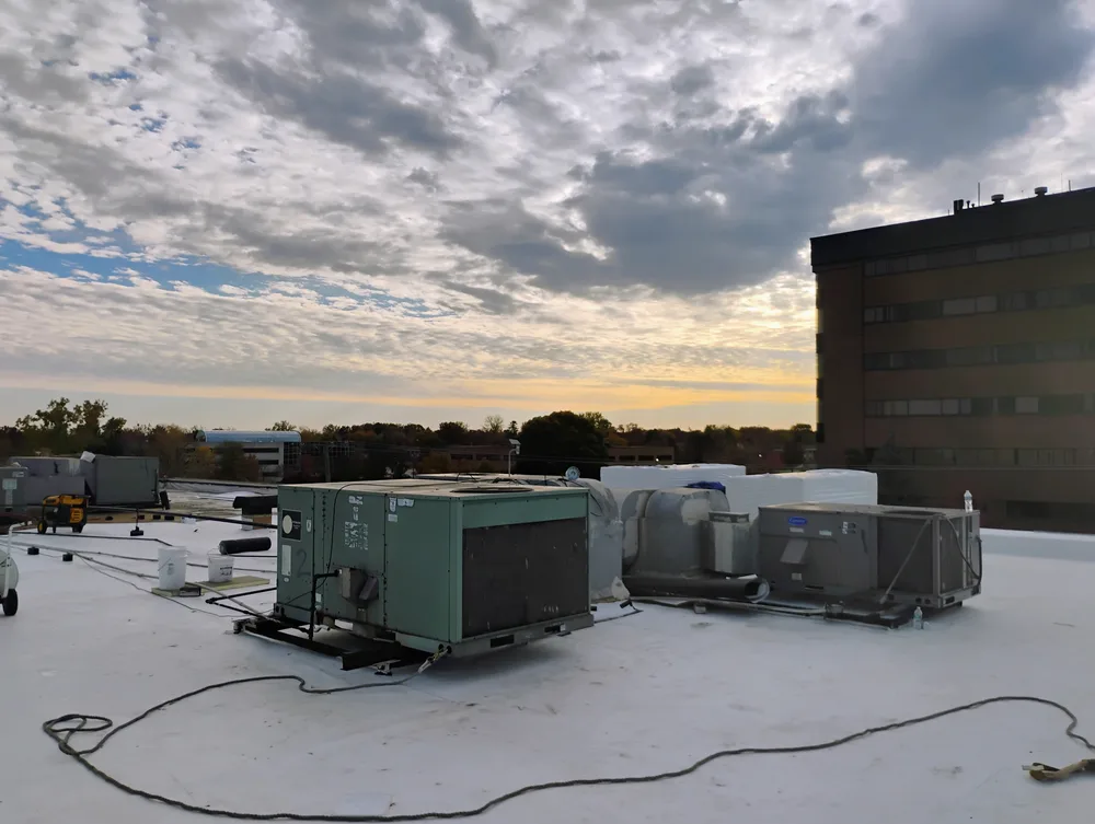 Large commercial TPO flat roof installation in Metro Detroit with rooftop HVAC units and city skyline at dusk