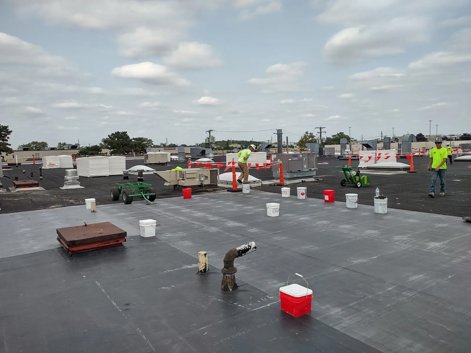 Full crew active on massive commercial EPDM flat roof installation with adhesive rollers and safety cones, Metro Detroit