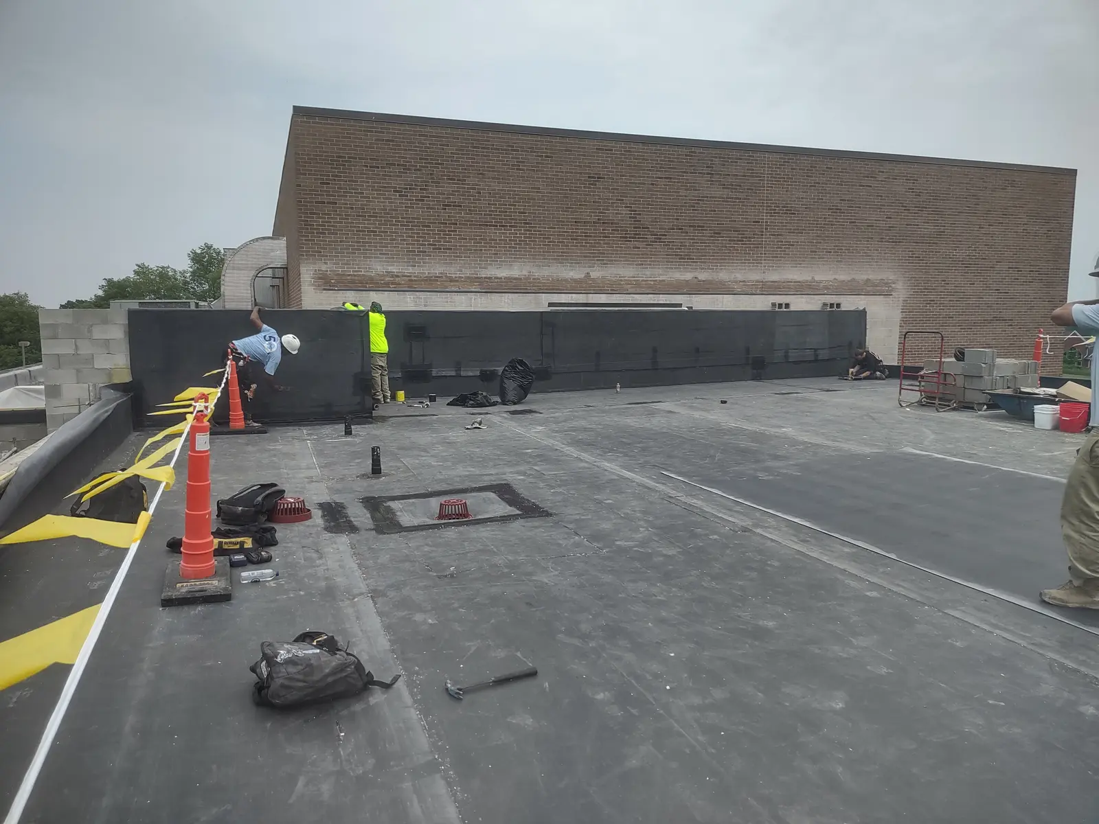 Crew installing EPDM membrane at parapet wall on commercial brick building flat roof, Metro Detroit