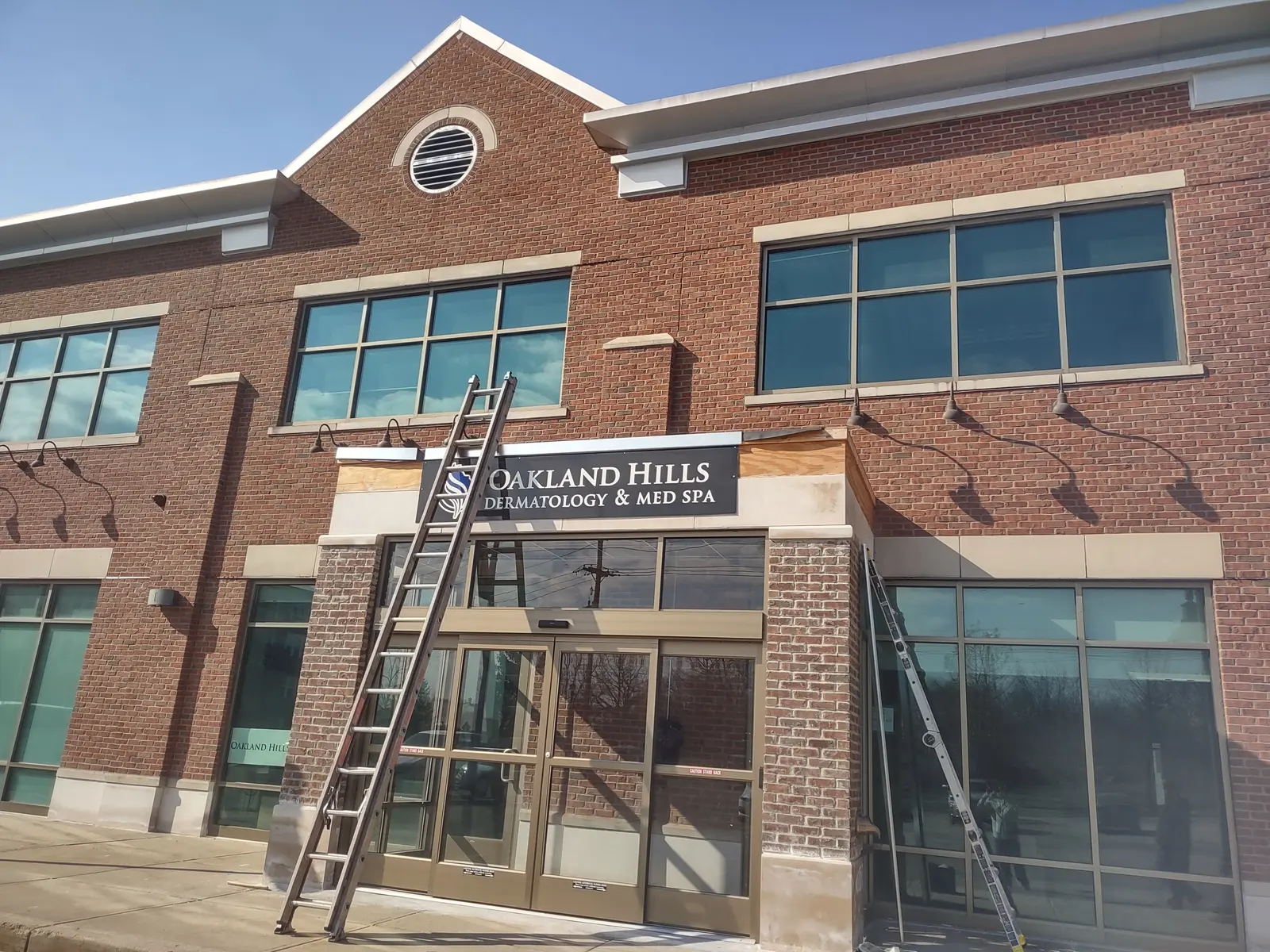 Ladders staged at brick storefront for commercial canopy roofing work, Oakland Hills area, Metro Detroit