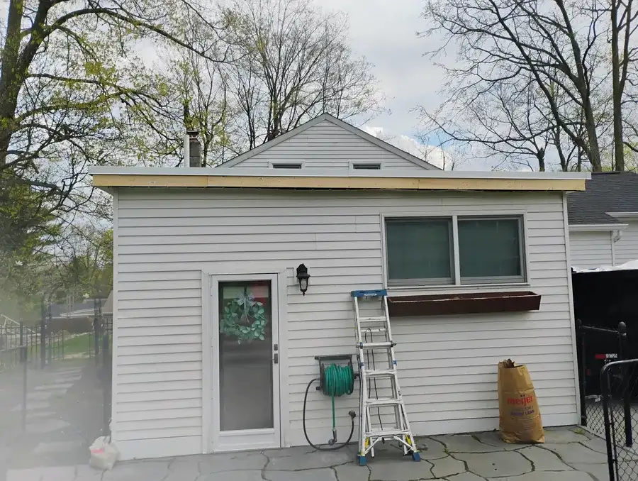 Front view of white-siding house with new fascia and drip edge installed before flat roof membrane