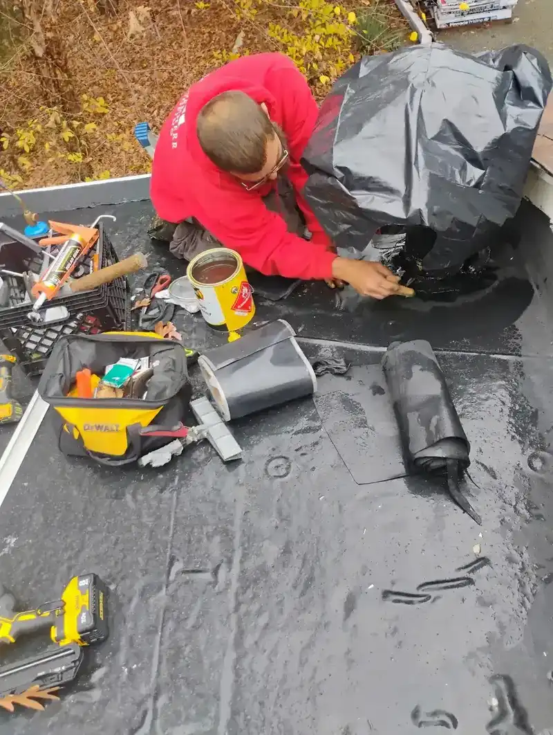Technician applying EPDM adhesive at pipe penetration during flat roof leak repair in Metro Detroit